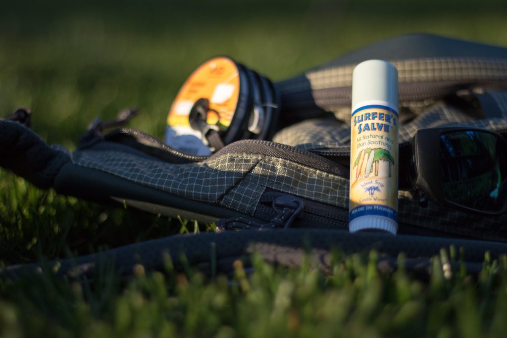 A stick of Surfer's Salve sitting against sunglasses and fly fishing gear