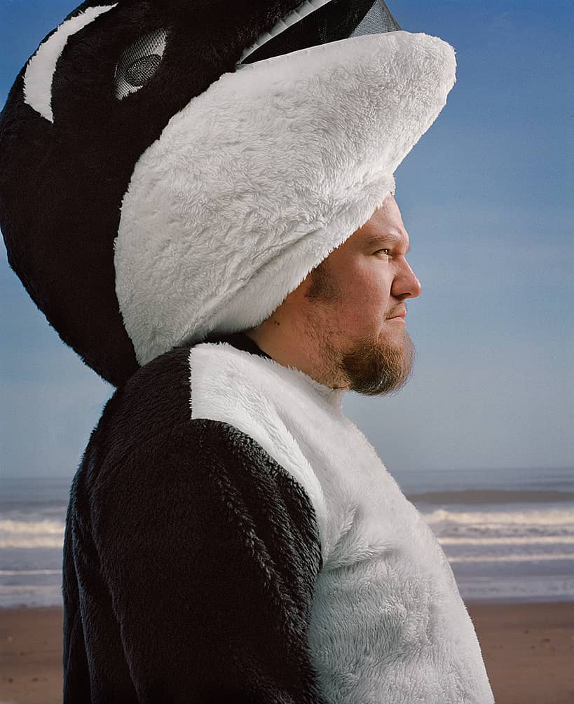 Erik Urdahl, founder of The Spout, standing on a beach wearing an orca costume