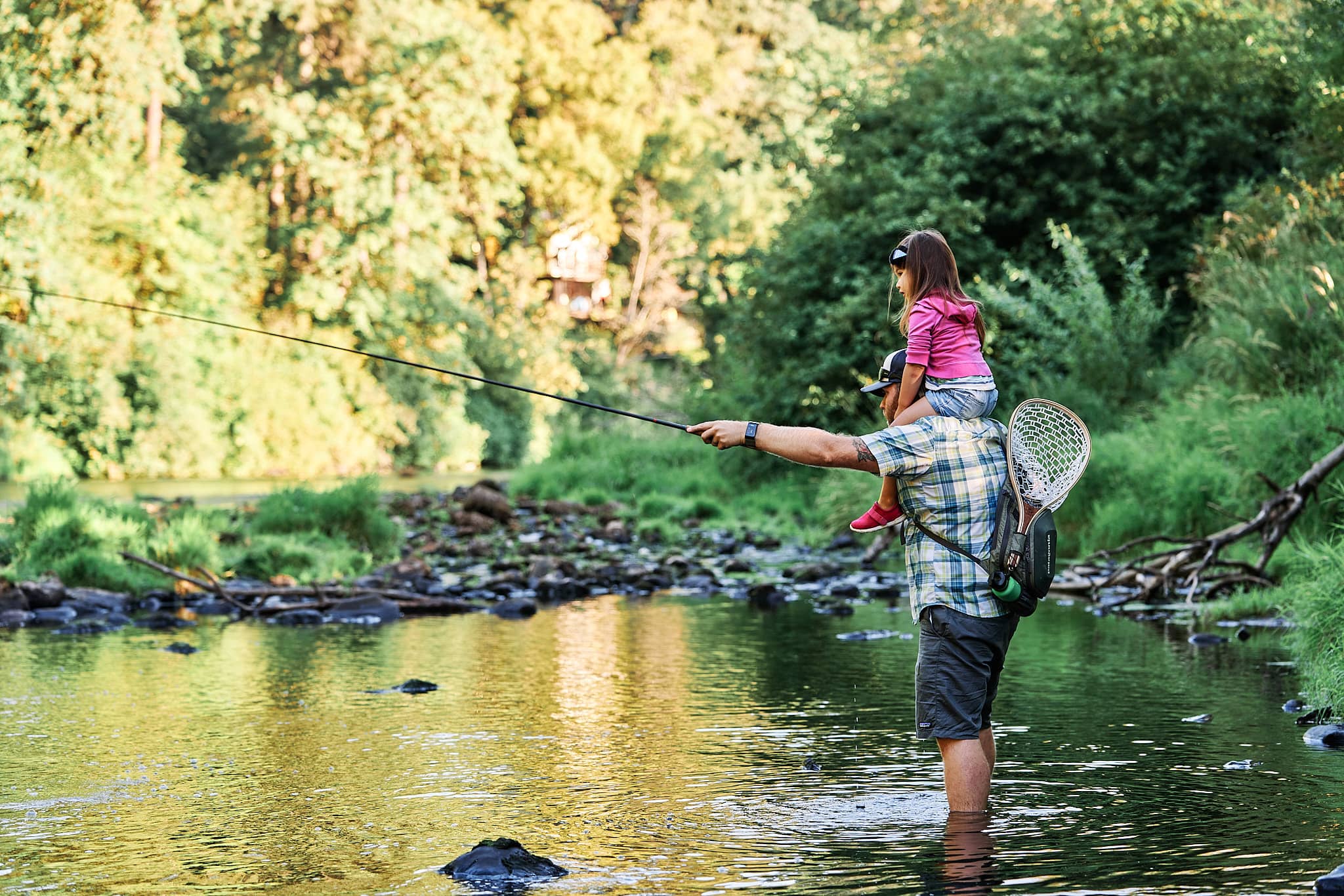 Dad holding a Tenkara rod straight out while his daughter watches from his shoulders