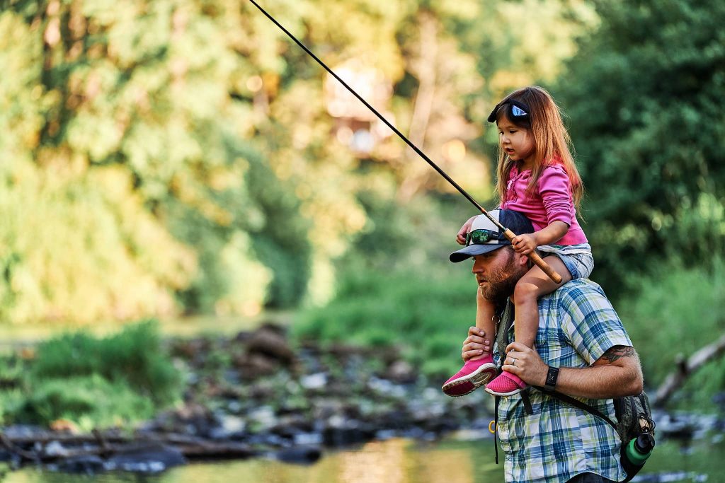 McKenzie holding a Tenkara rod in a river on Dad's shoulders