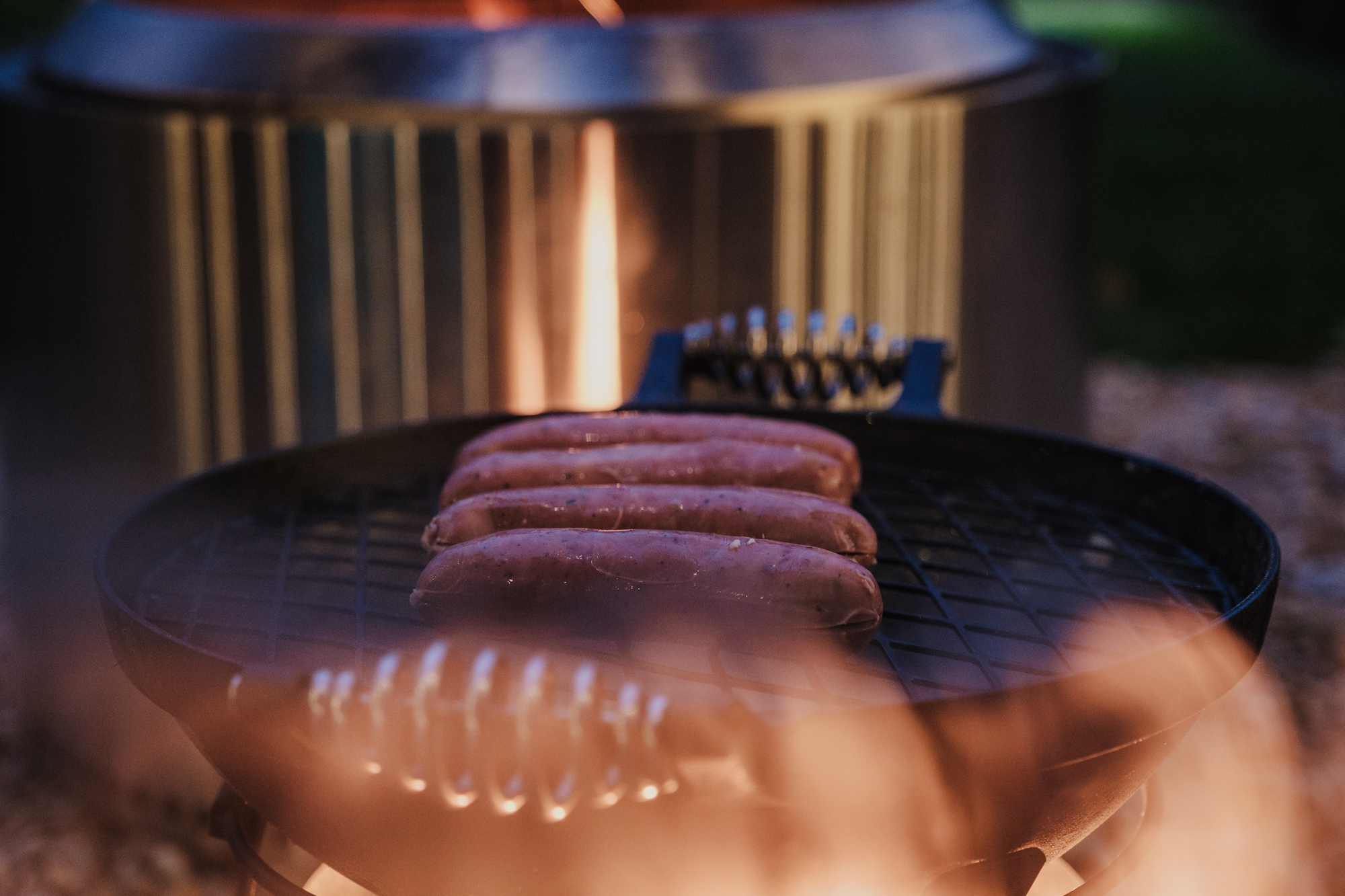 Sausages steaming on a Barebones Living All-In-One Cast Iron Grill grate