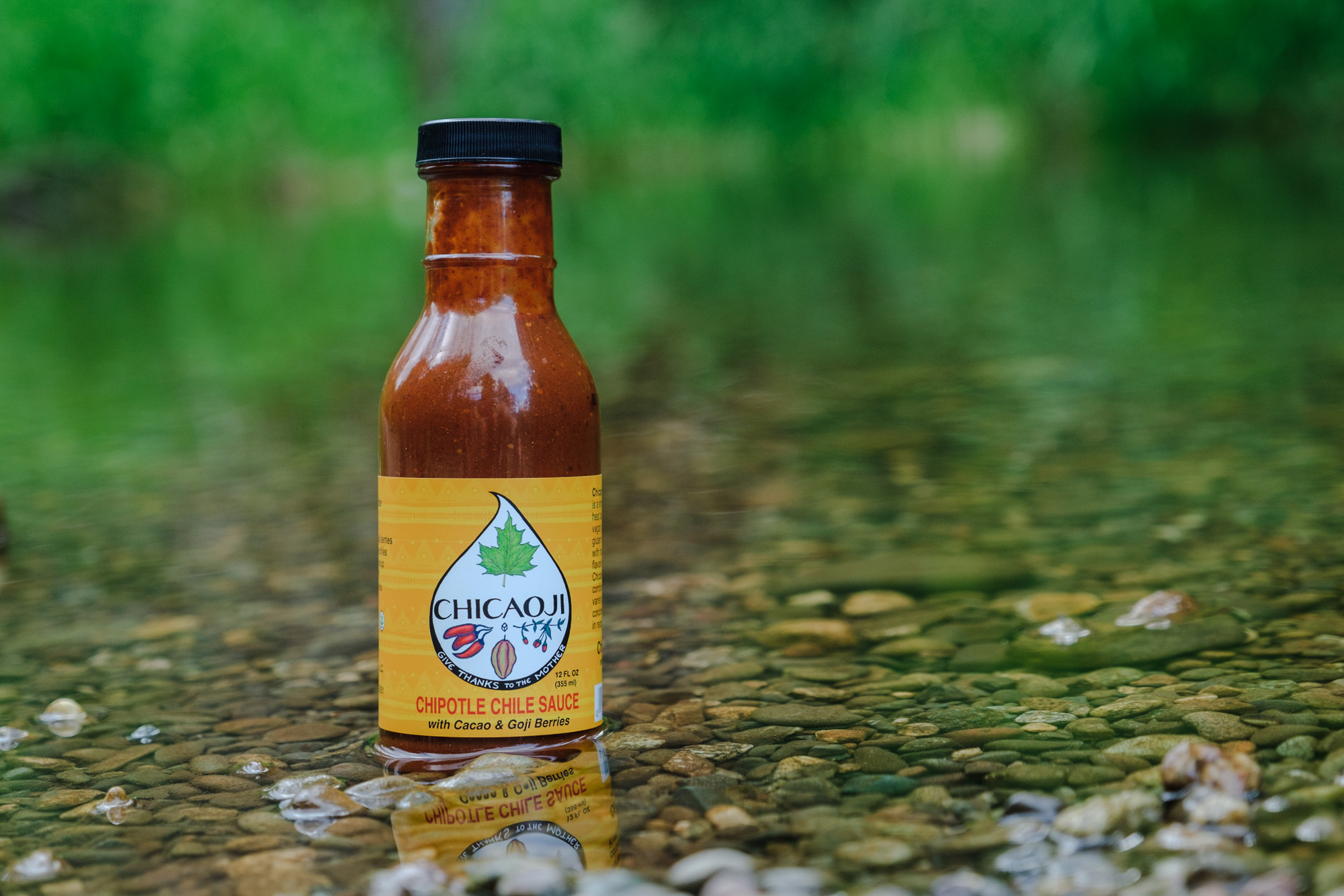 A bottle of Chicaoji sauce sitting on gravel a shallow river