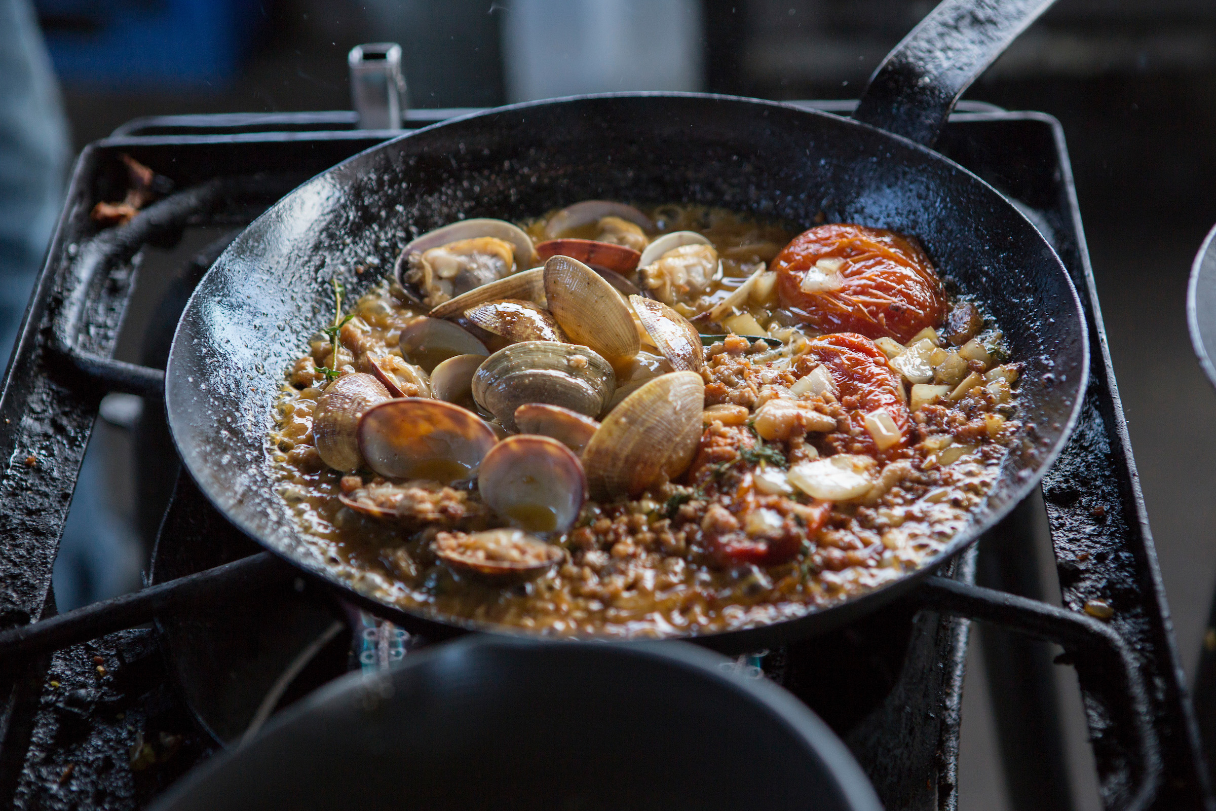 Clams steaming in a pan with beans and blistered tomatoes on a propane cooking ring