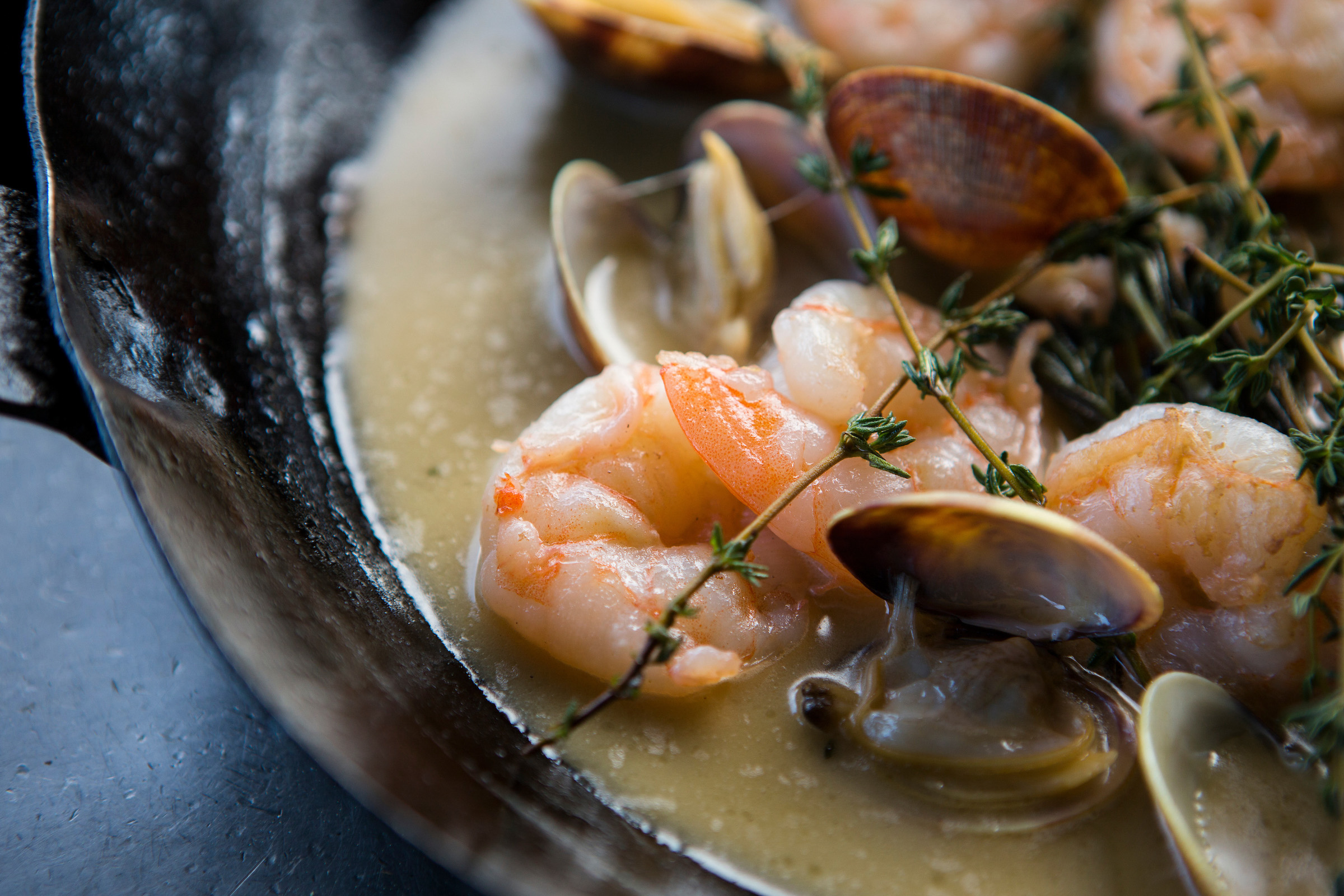 A closeup picture of cooked shrimp, steamed clams, fresh thyme, and broth in a bowl