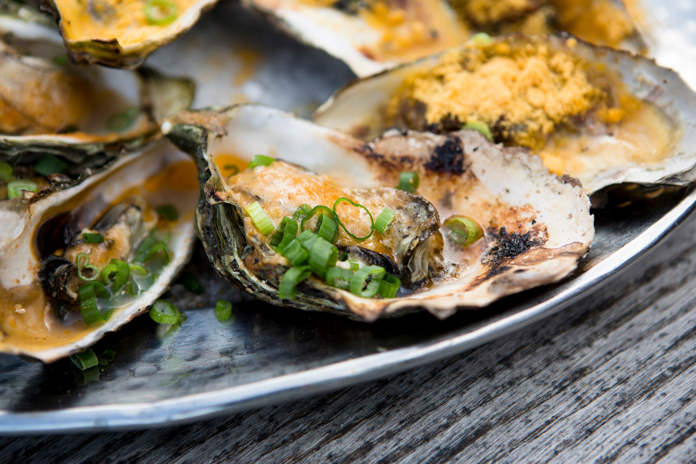A closeup picture of charred oysters topped with butter and green onions