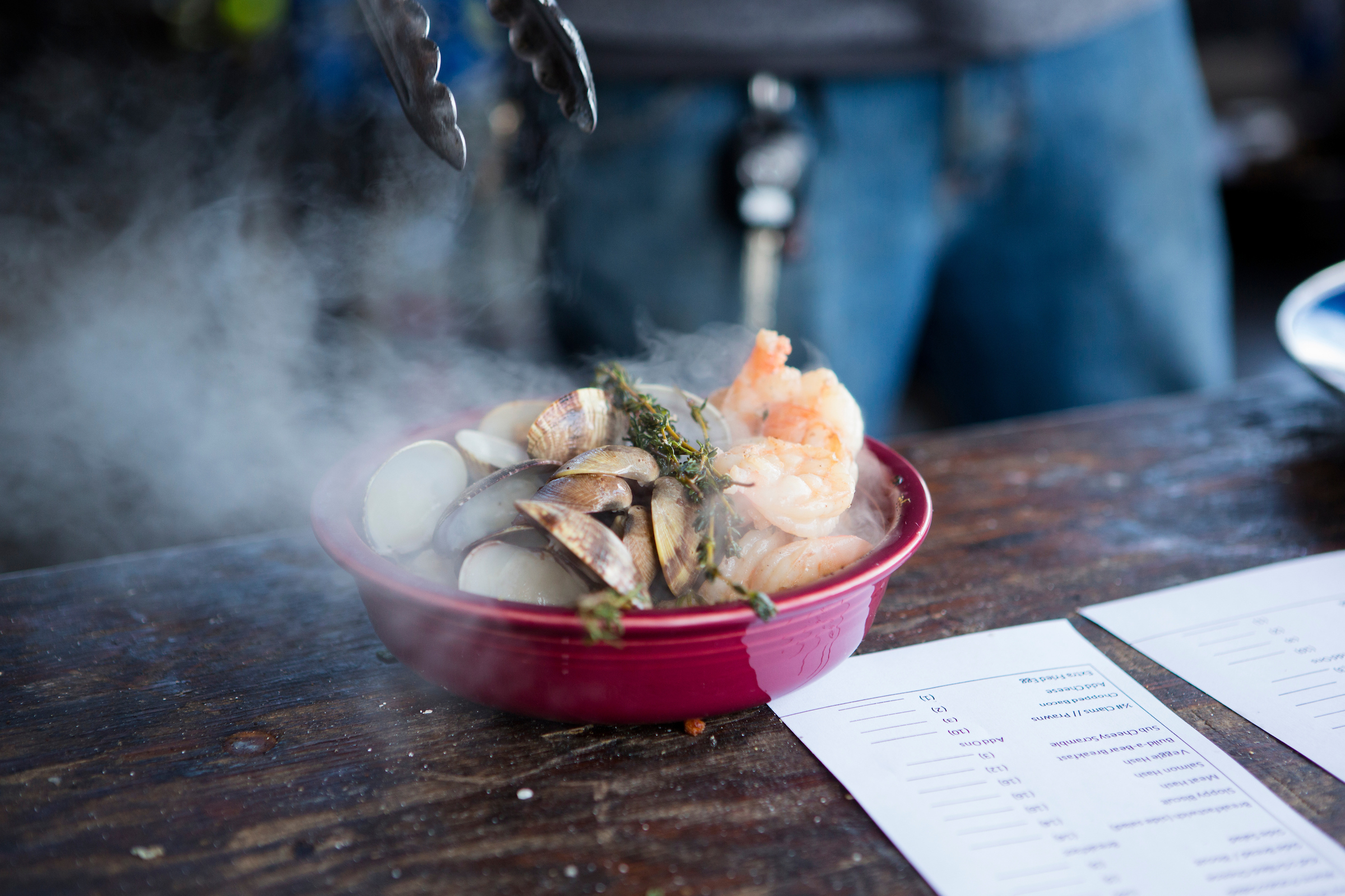 A red bowl full of steaming clams and shrimp on a wooden table