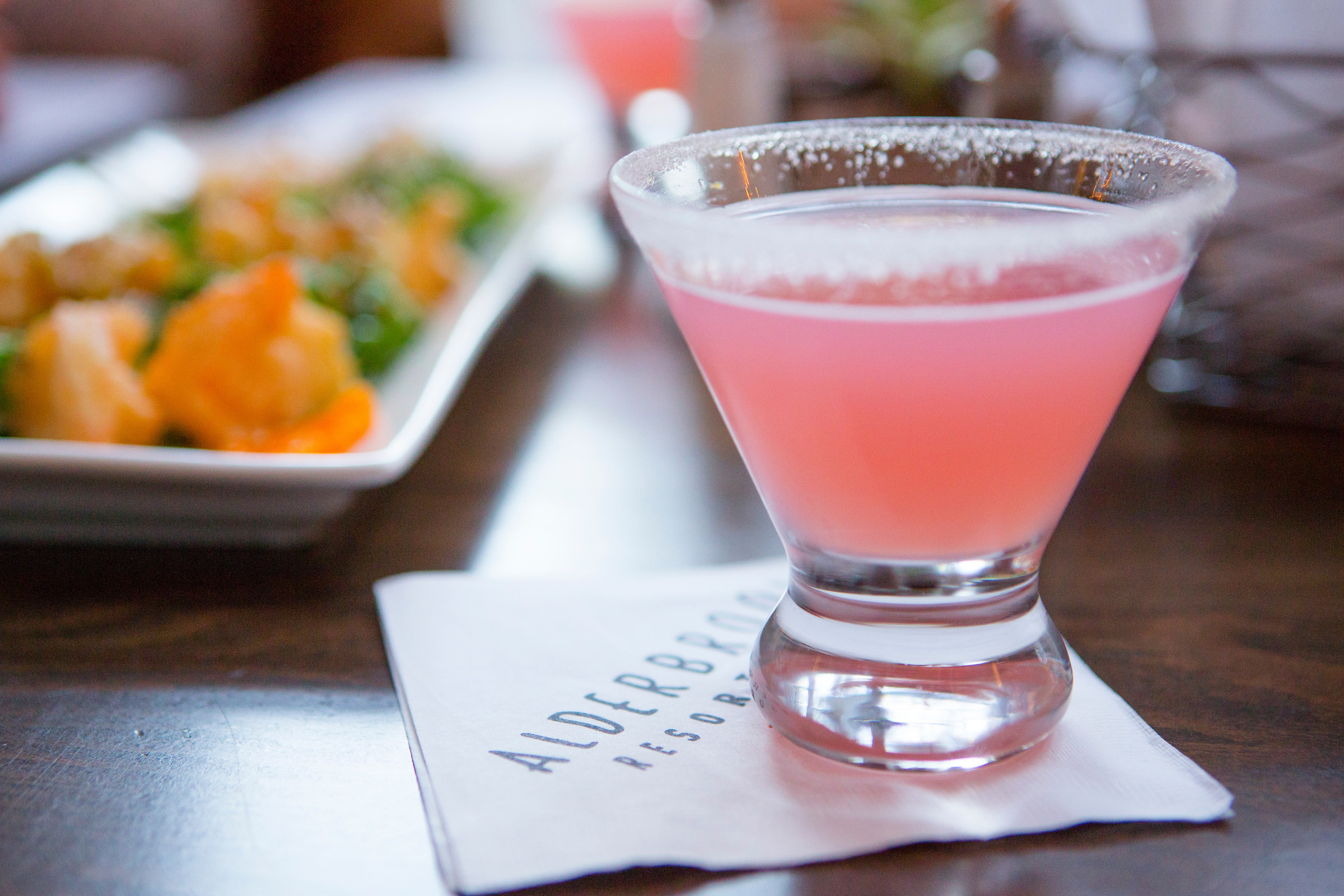 A pink cocktail in a sugar-rimmed glass sitting on a napkin that reads Alderbrook Resort & Spa