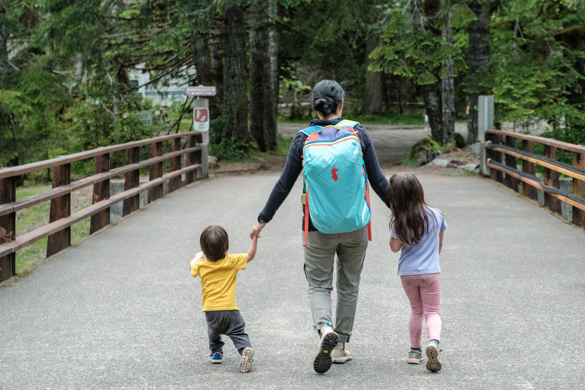 Woman wearing the Cotopaxi Allpa 35 while crossing a bridge with her young kids