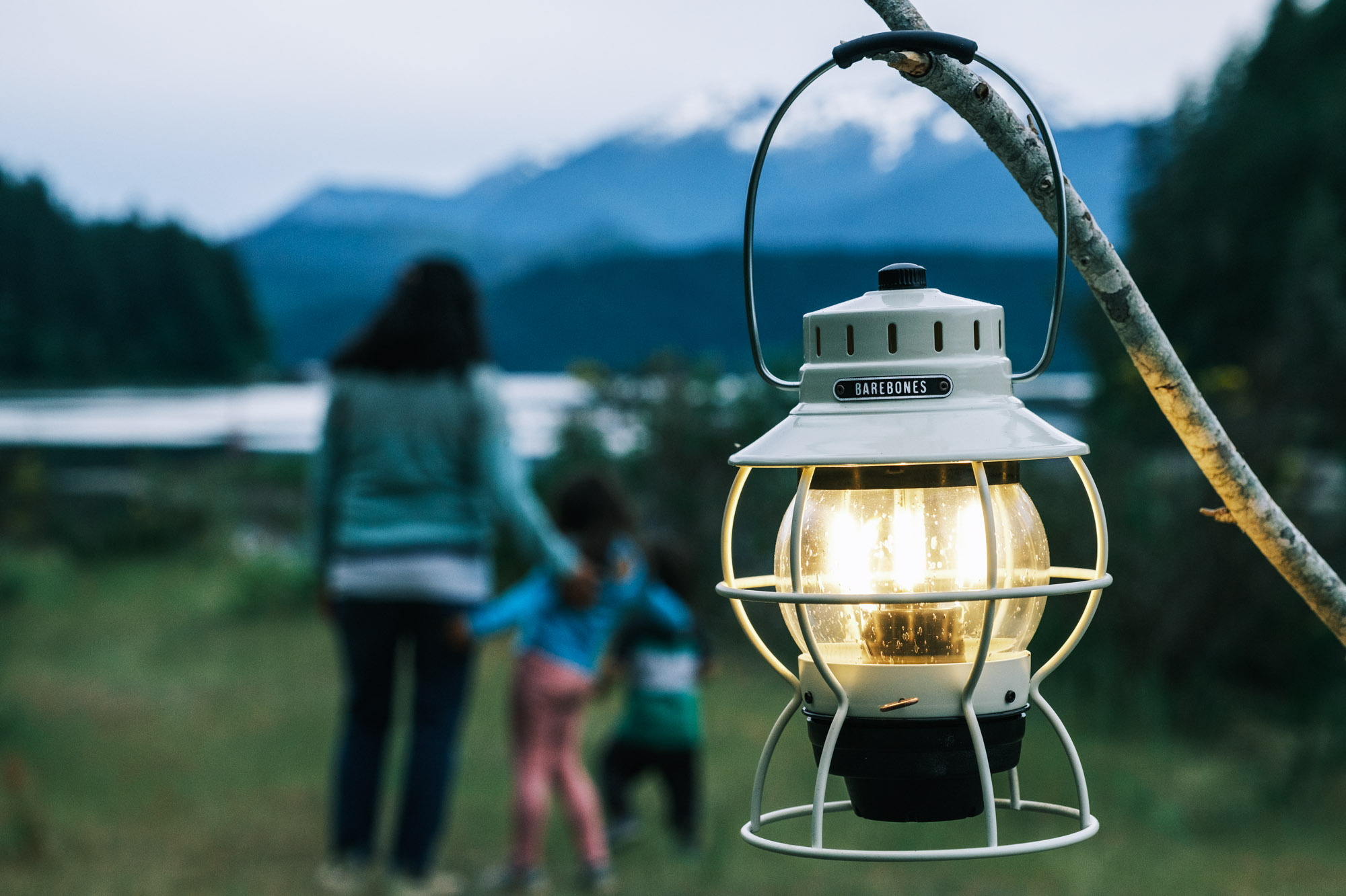 A vintage style rechargeable lantern hanging on a branch with a mother and her two children in the background