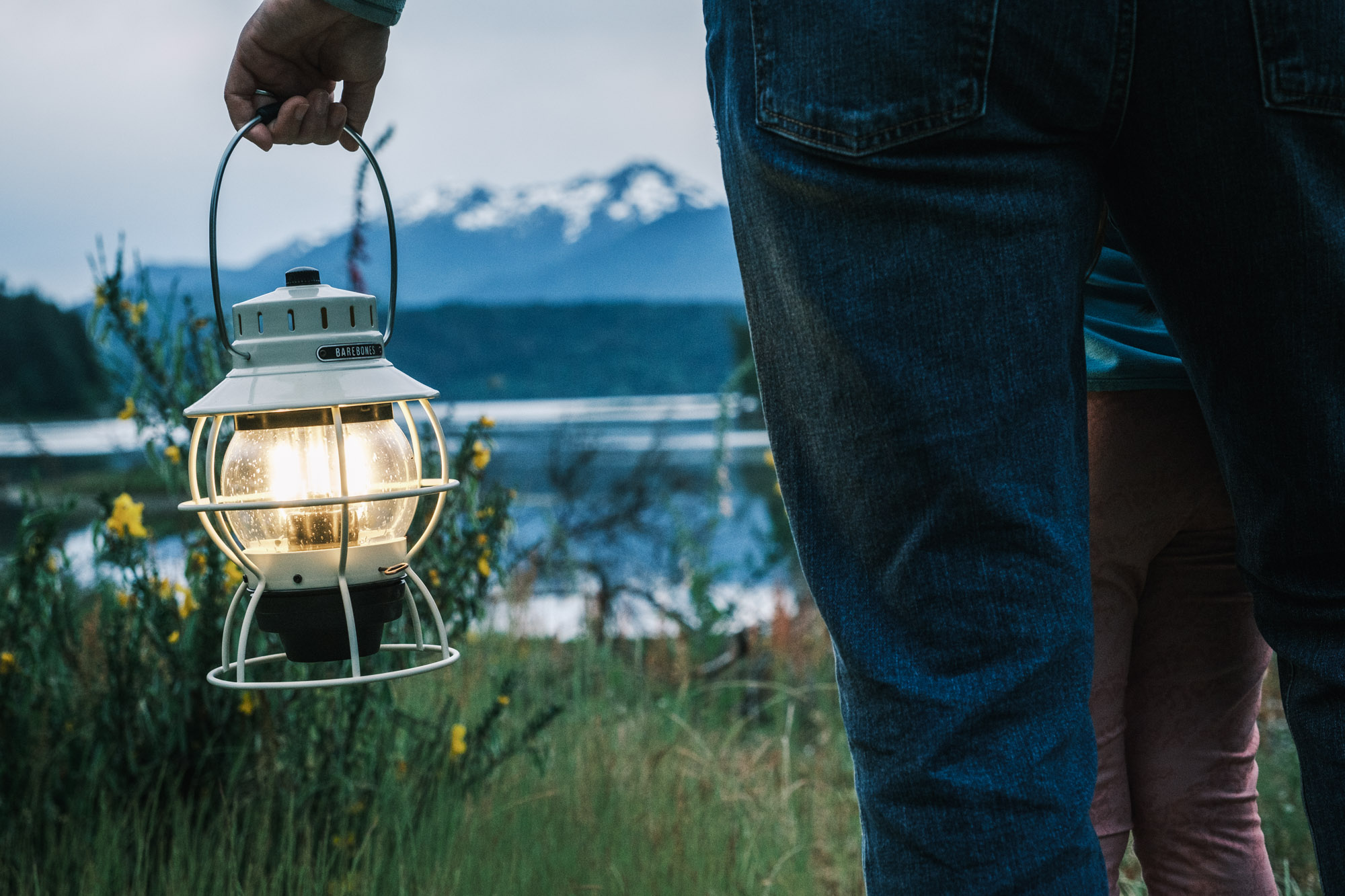 A woman carrying the Barebones vintage railroad lantern beneath snow covered mountains in the Pacific Northwest