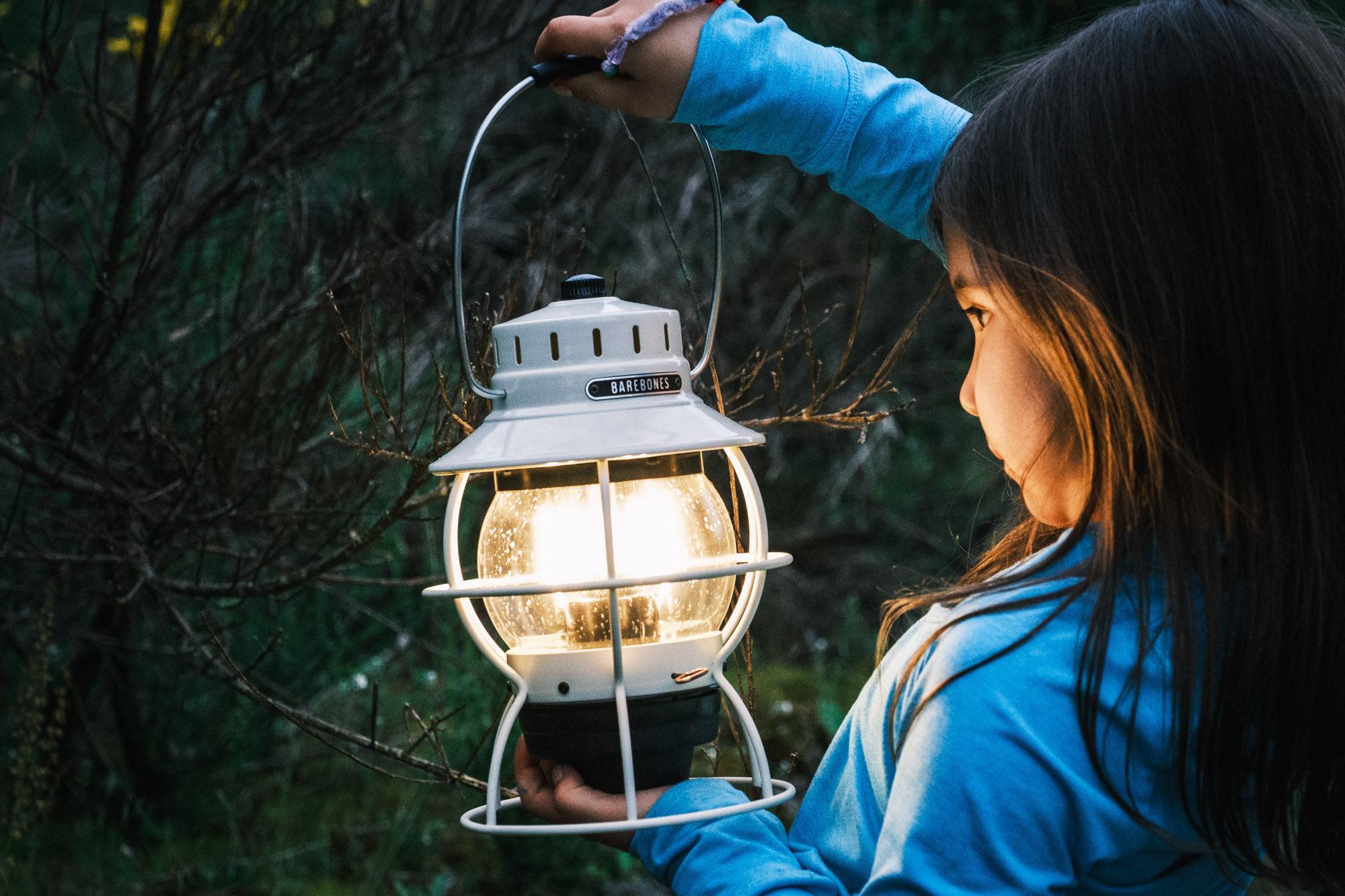 A young girl holding the Barebones Railroad LED Lantern close to her face