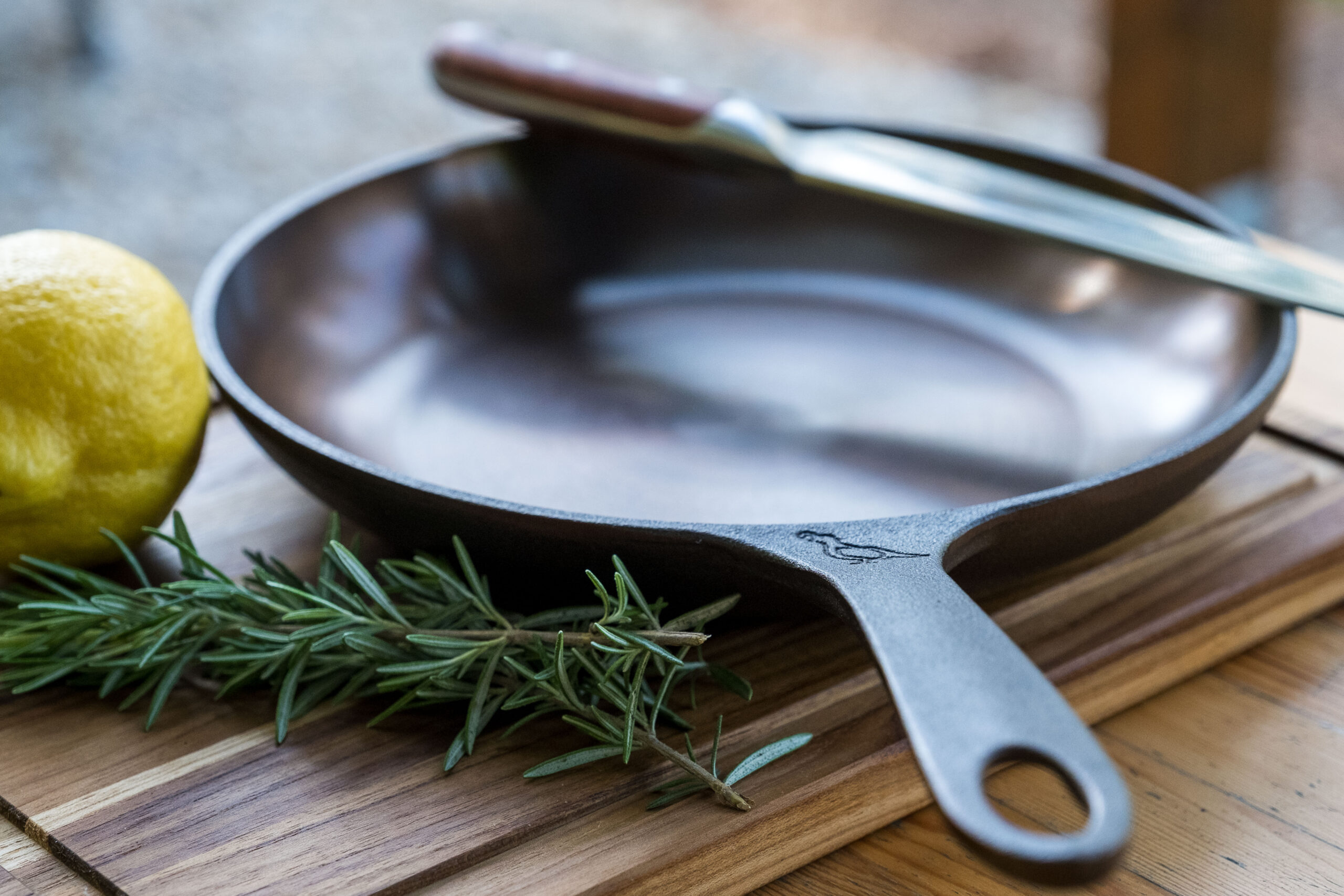 A lemon and a sprig of rosemary next to a cast iron skillet on a cutting board