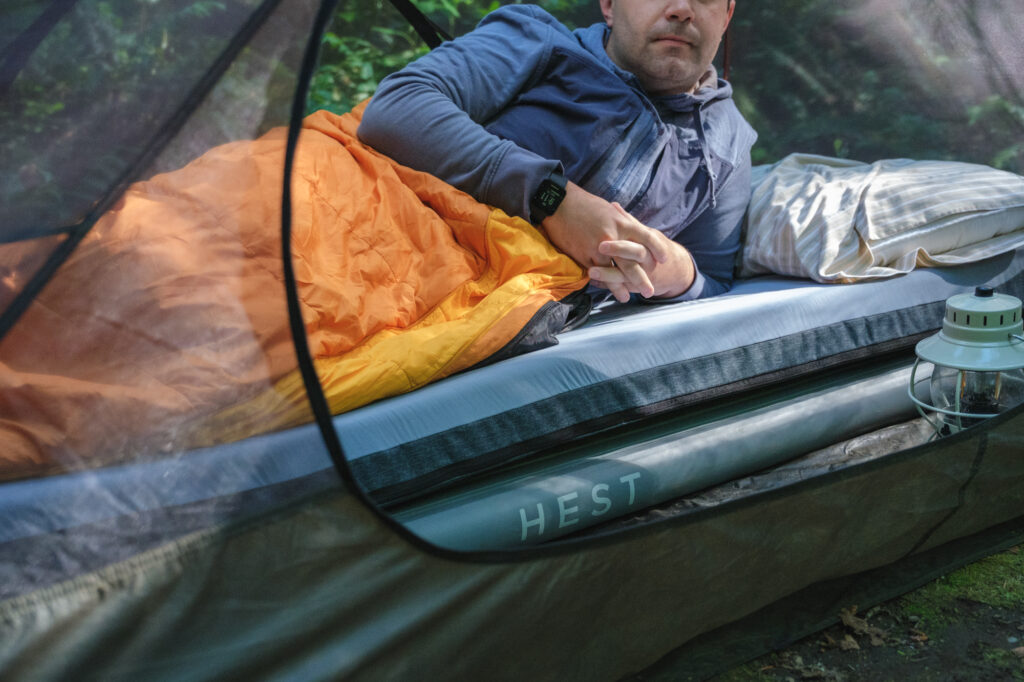 A man wrapped in an orange sleeping bag laying on his side on a Hest sleeping pad in a tent