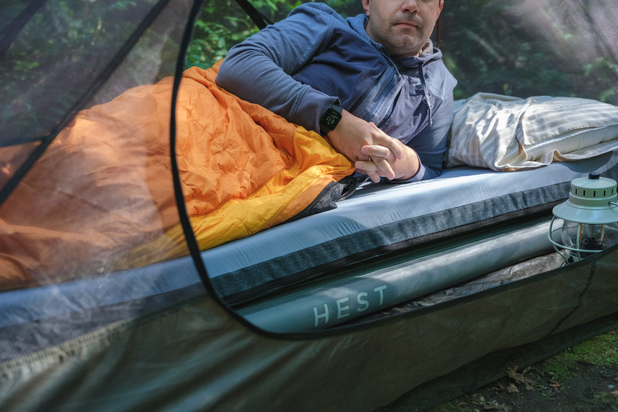 A man wrapped in an orange sleeping bag laying on his side on a Hest sleeping pad in a tent