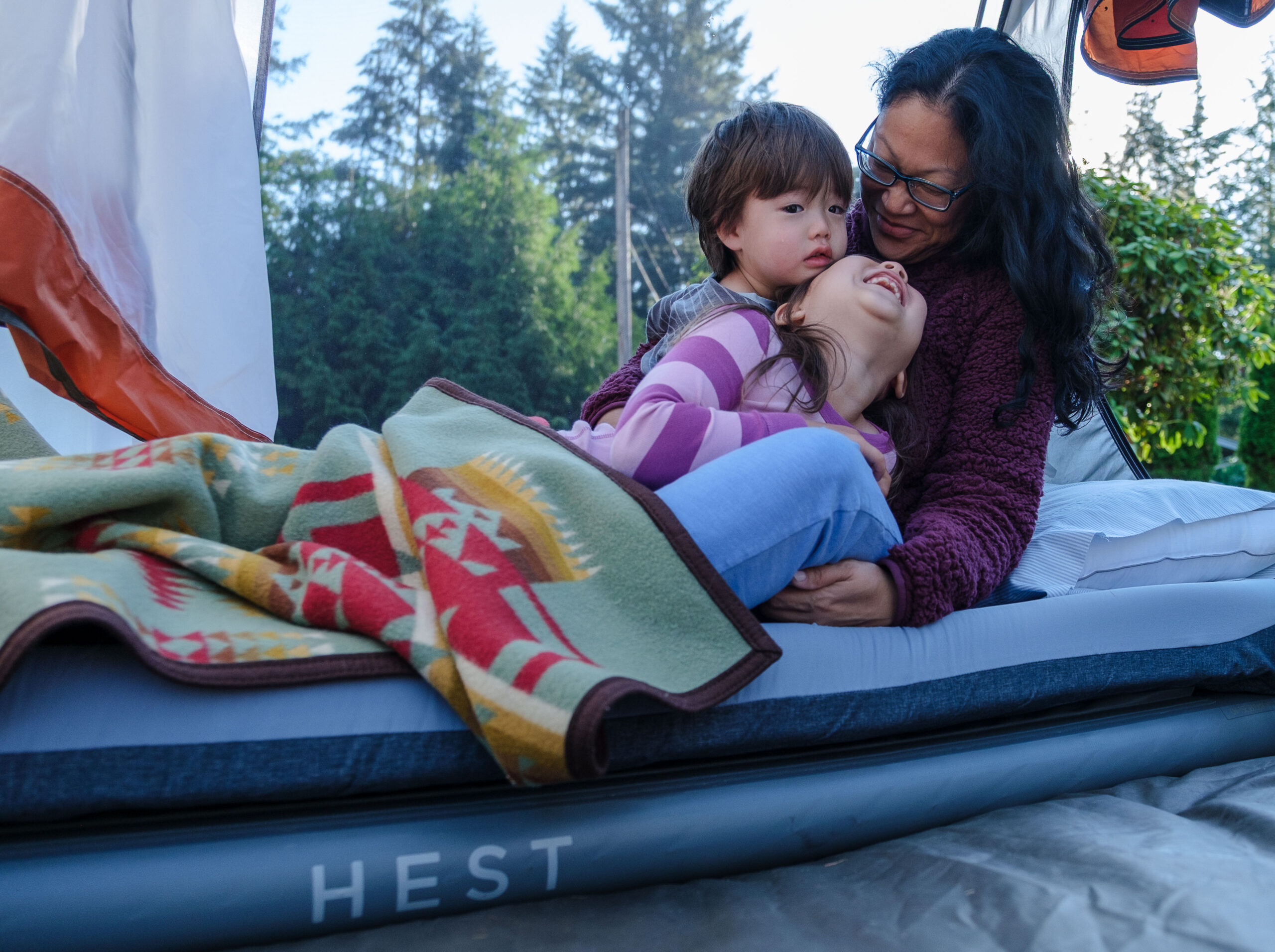 A mother and her two kids smiling and laying on a Hest Sleep System bed